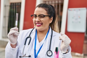 Young hispanic doctor woman doing coronavirus infection nasal test winking looking at the camera...