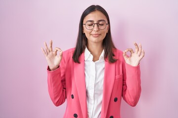 Young hispanic woman wearing business clothes and glasses relaxed and smiling with eyes closed doing meditation gesture with fingers. yoga concept.