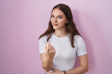 Fototapeta premium Young hispanic girl standing over pink background beckoning come here gesture with hand inviting welcoming happy and smiling