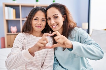 Woman and girl mother and daughter doing heart gesture with hands at bedroom