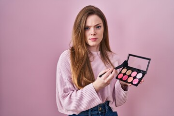 Young caucasian woman holding makeup brush and blush palette skeptic and nervous, frowning upset because of problem. negative person.