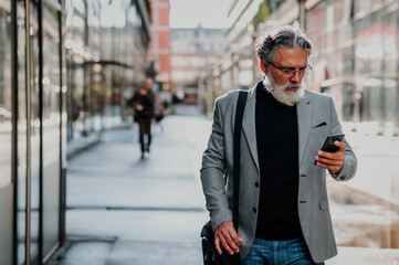 Senior businessman standing outside and using smartphone