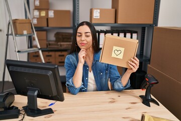 Hispanic woman working at small business ecommerce holding box serious face thinking about question...