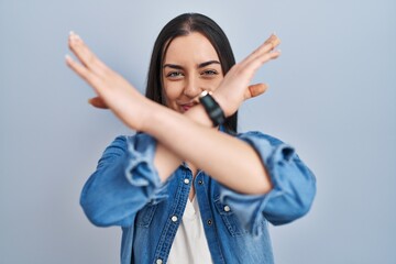 Hispanic woman standing over blue background rejection expression crossing arms doing negative sign, angry face