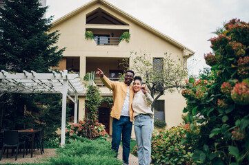 Multiracial couple holding keys and standing outside their new home
