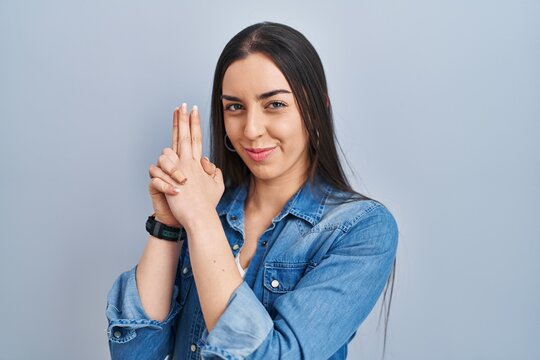 Hispanic woman standing over blue background holding symbolic gun with hand gesture, playing killing shooting weapons, angry face