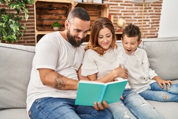 Family reading book sitting on sofa at home