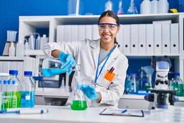 Young african american woman scientist pouring liquid at laboratory