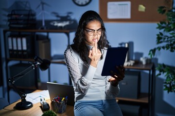 Young brazilian woman using touchpad at night working at the office showing middle finger, impolite...