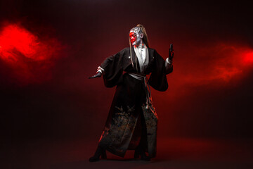 Naklejka premium A young woman in fantastic makeup and an Asian kimono, the image of a cyber geisha. Full - length photo , dancing on a dark background with red backlight