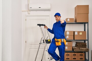 Young hispanic man working at renovation pointing with finger to the camera and to you, confident gesture looking serious