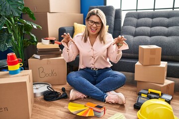 Young hispanic woman moving to a new home sitting on the floor smiling funny doing claw gesture as cat, aggressive and sexy expression