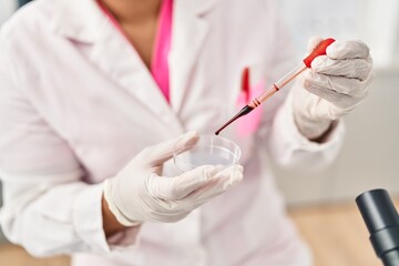 Young hispanic woman wearing scientist uniform analysing blood at laboratory
