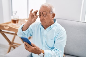 Senior grey-haired man using smartphone sitting on sofa at home