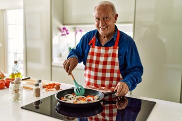 Senior man smiling confident cooking at kitchen