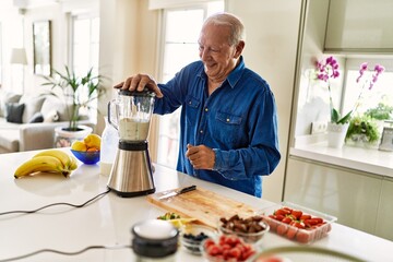 Senior man smiling confident shaking blender at kitchen