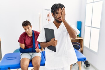 Young hispanic man working at pain recovery clinic with a man with broken arm yawning tired covering half face, eye and mouth with hand. face hurts in pain.