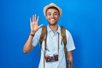 Brazilian young man holding vintage camera showing and pointing up with fingers number five while smiling confident and happy.