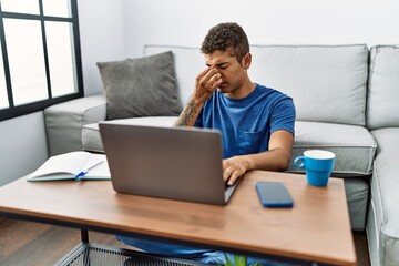 Young handsome hispanic man using laptop sitting on the floor tired rubbing nose and eyes feeling fatigue and headache. stress and frustration concept.