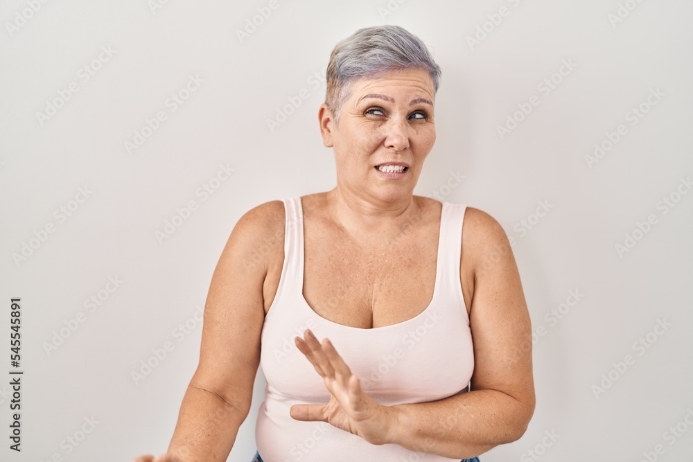 Poster Middle age caucasian woman standing over white background disgusted expression, displeased and fearful doing disgust face because aversion reaction. with hands raised