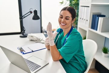 Young beautiful hispanic woman doctor smiling confident wearing gloves at clinic