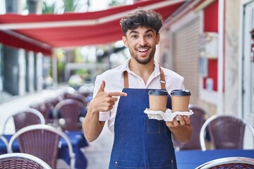 Arab man with beard wearing waiter apron at restaurant terrace smiling happy pointing with hand and...