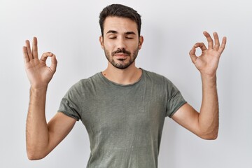 Young hispanic man with beard wearing casual t shirt over white background relax and smiling with eyes closed doing meditation gesture with fingers. yoga concept.