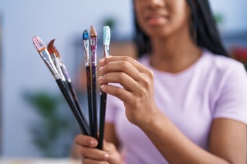 African american woman artist smiling confident holding paintbrushes at art studio