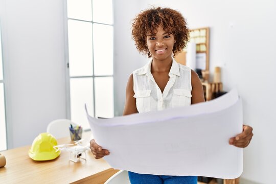 Young african american woman smiling confident holding blueprints at architecture studio - Powered by Adobe