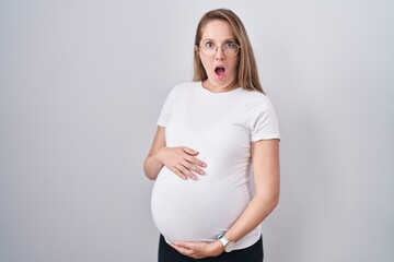 Young pregnant woman expecting a baby, touching pregnant belly afraid and shocked with surprise and...