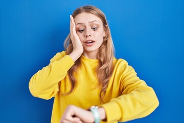 Young caucasian woman standing over blue background looking at the watch time worried, afraid of...