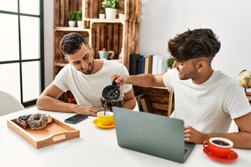 Fototapeta na wymiar Two hispanic men couple pouring coffee having breakfast at home