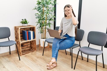 Young asian nurse woman sitting at waiting room using laptop smiling happy doing ok sign with hand on eye looking through fingers