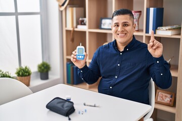 Hispanic young man holding glucometer device surprised with an idea or question pointing finger...