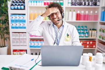 Naklejka na ściany i meble Hispanic young man working at pharmacy drugstore working with laptop stressed and frustrated with hand on head, surprised and angry face