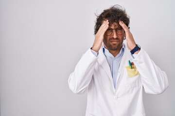 Hispanic young man wearing doctor uniform with hand on head for pain in head because stress. suffering migraine.