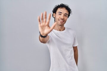 Hispanic man standing over isolated background showing and pointing up with fingers number five while smiling confident and happy.