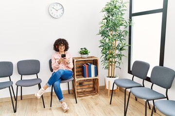 Young middle east woman listening to music sitting on chair at waiting room