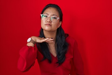 Asian young woman standing over red background cutting throat with hand as knife, threaten aggression with furious violence