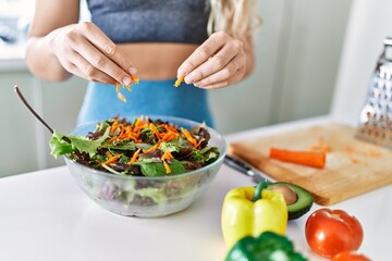 Young woman pouring carrot on salad at kitchen