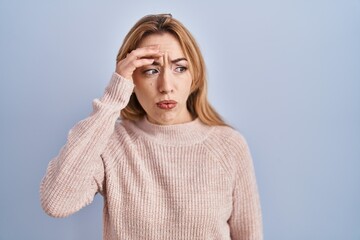 Hispanic woman standing over blue background worried and stressed about a problem with hand on forehead, nervous and anxious for crisis