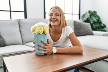 Young blonde woman smiling confident smelling flowers at home
