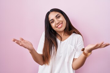 Young arab woman standing over pink background smiling cheerful offering hands giving assistance and acceptance.