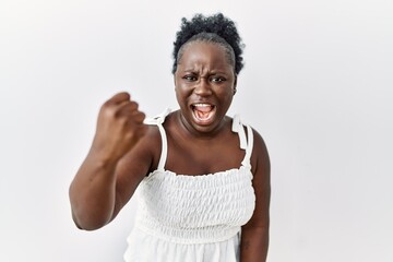 Young african woman standing over white isolated background angry and mad raising fist frustrated...