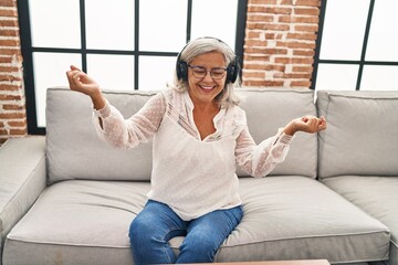 Fototapeta premium Middle age woman listening to music sitting on sofa at home