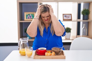 Obraz na płótnie Canvas Caucasian plus size woman eating breakfast at home suffering from headache desperate and stressed because pain and migraine. hands on head.