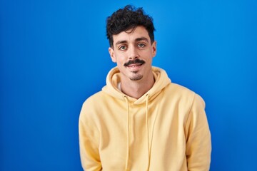 Hispanic man standing over blue background with a happy and cool smile on face. lucky person.