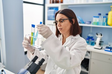 Young beautiful hispanic woman scientist holding test tubes at laboratory