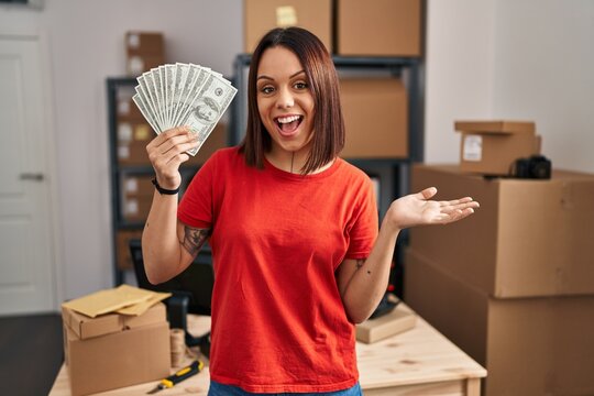 Young hispanic woman working at small business ecommerce holding banknotes celebrating achievement with happy smile and winner expression with raised hand