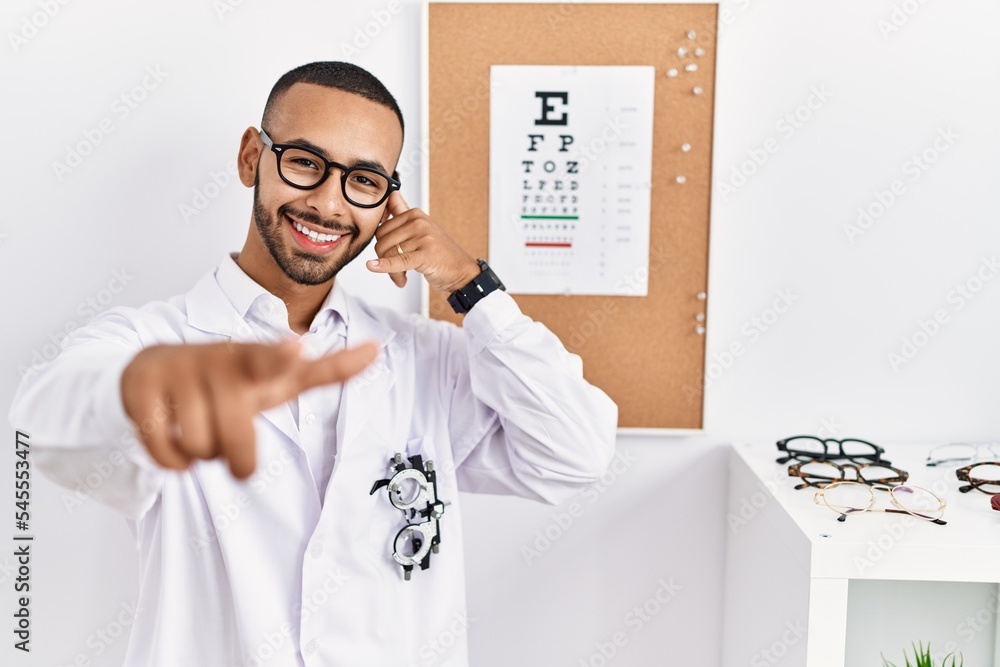 Canvas Prints African american optician man standing by eyesight test smiling doing talking on the telephone gesture and pointing to you. call me.